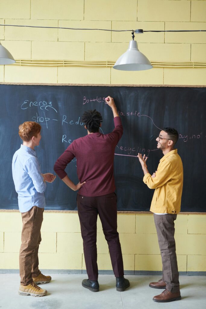 Three adults discussing strategies at a chalkboard in a modern office space.